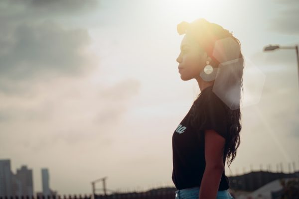 阳光照进窗户的咖啡馆内，一名年轻女性正专注地用耳机听英语音频并做笔记，桌上放着手机和分级读物，学习氛围轻松高效